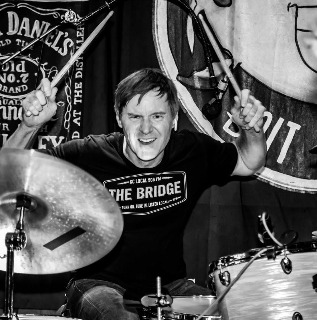 Scot Eldridge raising drumsticks behind a drum kit onstage